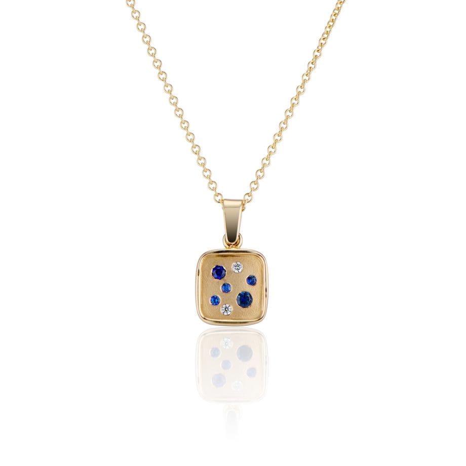 A galaxy of Diamonds and natural blue Sapphires sparkle in this 14K gold Brown Goldsmiths original cushion shaped pendant.