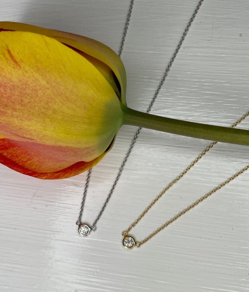 Graduation gift ideas. Diamond solitaire bezel Pendant Necklaces in yellow gold and 1 in white gold shown with a tulip