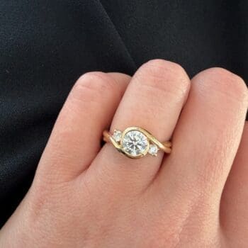 1.01ct round diamond bezel set engagement ring in 14K yellow gold with two smaller bezel-set diamonds