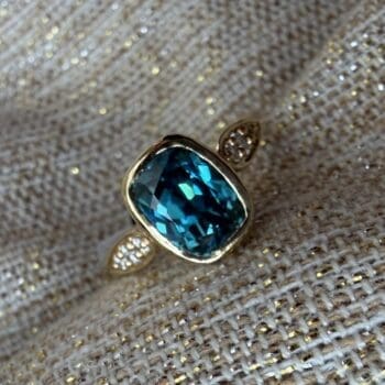 Concerto ring featuring a teal blue zircon center and elongated cushion cut gemstones in 14K yellow gold, size 6.5